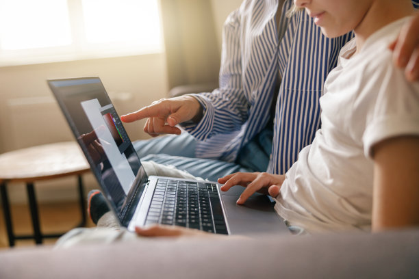 特写妈妈和儿子坐在沙发上，在笔记本电脑上做作业。远程在线教育图片下载