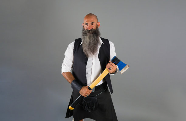 一个留着长胡子的光头男子站在灰色背景前，手里拿着斧头，看着镜头图片下载
