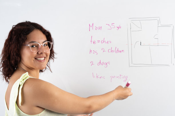 偷拍的年轻女子微笑着，一边看着镜头，一边用粉红色的马克笔解释白板上写的是什么。图片下载