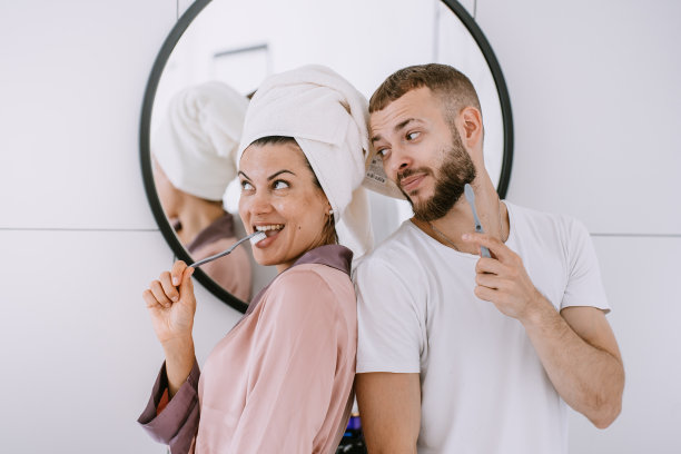 俏皮的西班牙年轻夫妇在浴室刷牙牙齿微笑拥抱。新婚夫妇在酒店房间享受蜜月。漂亮的白人女孩头上有毛巾和男朋友玩。图片下载