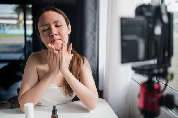 亚洲女性网红演示如何在脸上涂抹面霜和保湿霜，拍摄并流到社交媒体、美容博主和网红概念上。图片下载