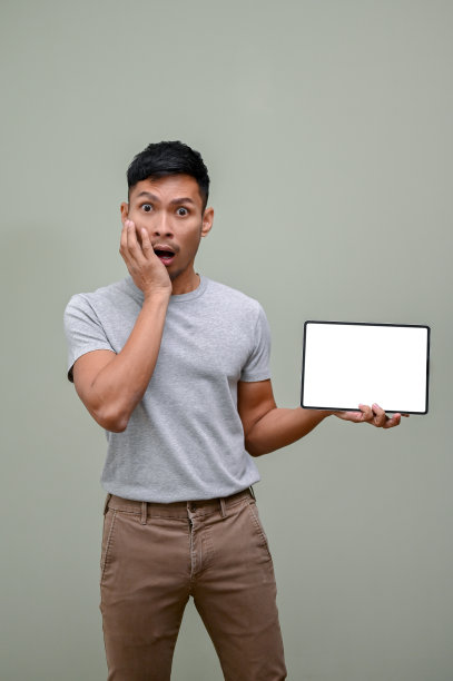 震惊和兴奋的亚洲男子捂着脸颊，拿着一个平板电脑模型图片下载