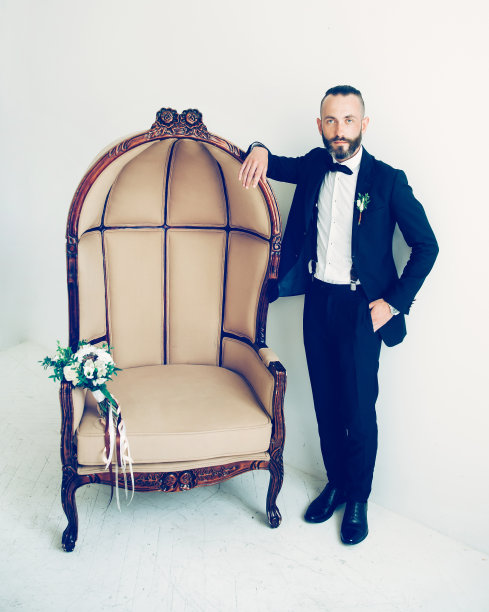 优雅的新郎站在酒店房间的椅子旁。图片下载