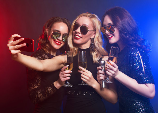 一群聚会的女性朋友用起泡酒敲着笛子，拿着麦克风和手机。图片下载