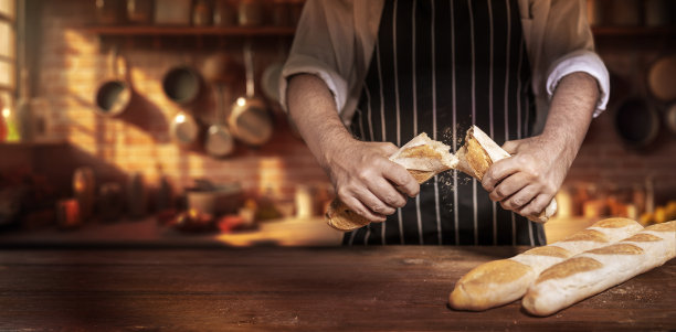 厨师在老式厨房的木桌上把长棍面包掰成两半图片下载