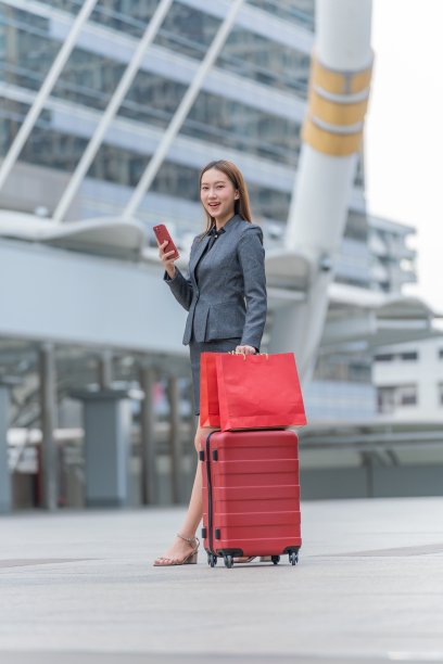 年轻优雅的亚洲女商人在完整的办公套装去出差。一边看手机一边经过一个CBD区域。图片下载