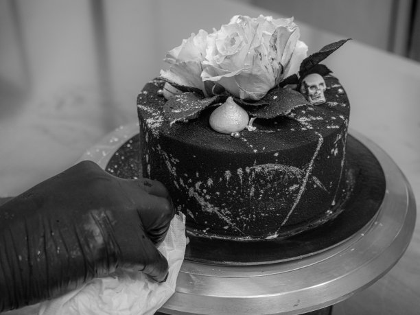 厨师浇上黑色喷枪画的糖霜蛋糕顶部两个真正的玫瑰银喷和可食用的巧克力骷髅图片下载
