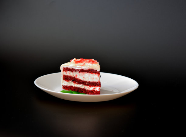 白色陶瓷盘子和一块蛋糕黑色天鹅绒装饰薄荷叶在黑色背景。图片下载