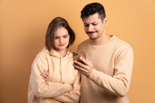 担心的夫妇在米色背景下用智能手机看视频和照片。通信、应用、连接概念。图片下载
