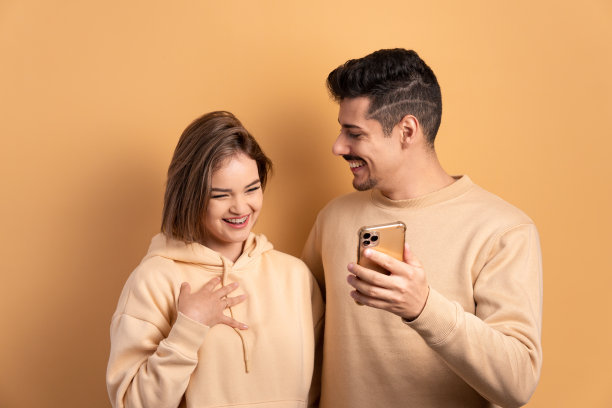 兴奋的情侣正在用米色的智能手机观看视频和照片。通信、应用、连接概念。图片下载
