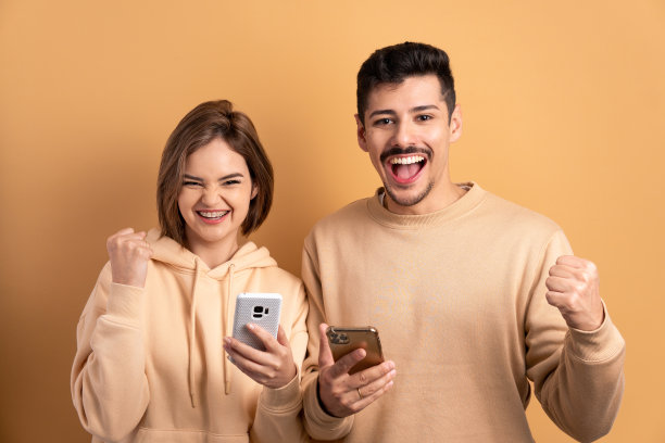 有趣的情侣在米色的工作室背景下观看智能手机上的视频和照片。网络，信息传递，互联网概念。图片下载