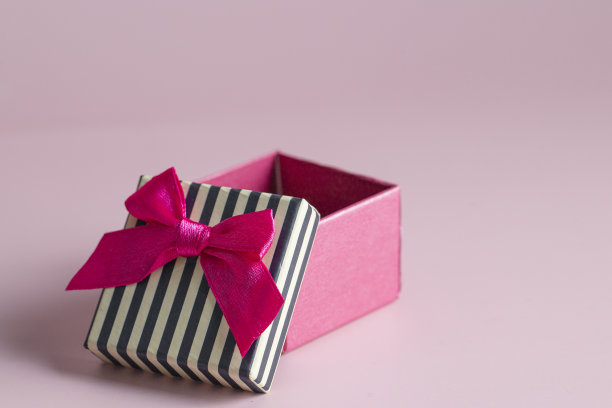 打开粉红色盒子与黑色的柄和红色的蝴蝶结在粉红色的背景图片下载