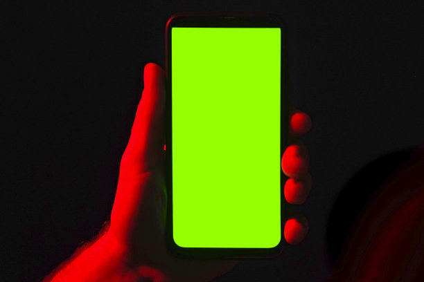年轻人手里拿着手机。使用智能手机，红蓝霓虹灯，绿色屏幕，深色背景。男性显示黑色手机色度键显示。关闭了。手举起装置，保持静止图片下载