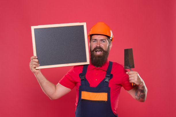 专业的泥水匠。熟练的泥水匠。成功的改造。带抹灰工具的大胡子工人。戴着安全帽的泥瓦匠时髦的建筑工人保持黑板复制空间。创造完美的表面图片下载