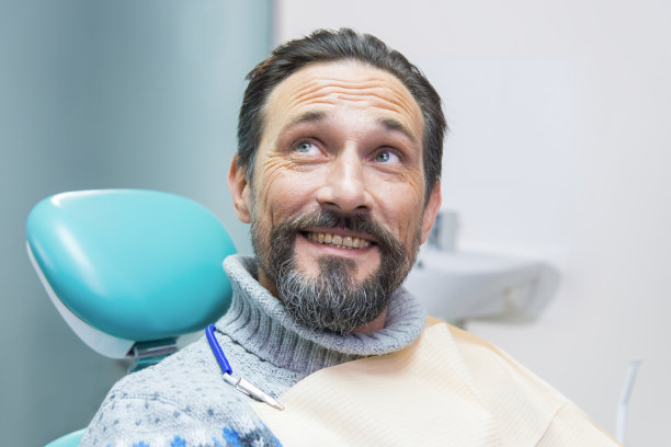 坐在牙科椅上的男人微笑着。图片下载