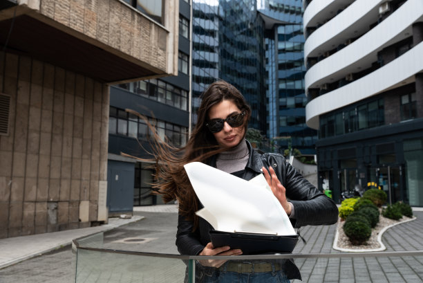 身穿皮夹克的酷岩女商人站在公司大楼外的小互联网公司老板。女商人戴着太阳镜在城市街道附近的办公楼图片下载
