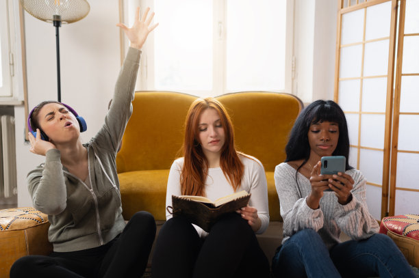 三个不同种族的女性舒适地坐在客厅的地板上。他们聚在一起，但被技术隔开，每个人都在做不同的事情。沟通和社会问题的概念。图片下载