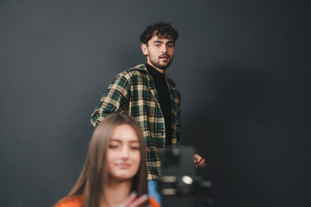 一对快乐的小情侣站在黑色背景下用手机拍摄视频。流媒体视频。图片下载