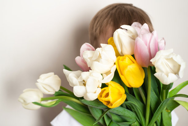 小男孩拿着一束五颜六色的郁金香放在面前。图片下载