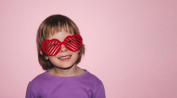 孩子穿着紫色t恤，戴着粉色背景的心形眼镜图片下载