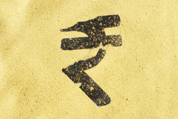 沙滩上立着一块石头做的印度卢比标志。国家货币符号的特写。金钱是靠不住的。商业和金融状况不稳定。图片下载