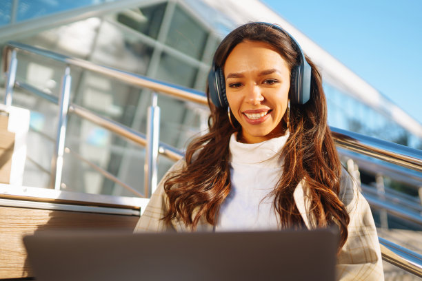 年轻女子戴着耳机，拿着笔记本电脑走在城市的街道上。图片下载