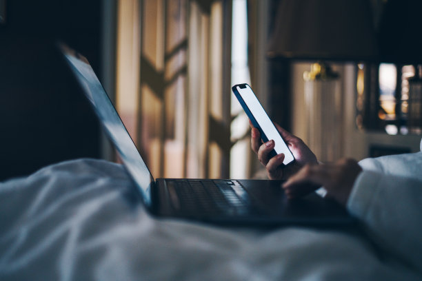 女人晚上在床上使用笔记本电脑和智能手机图片下载