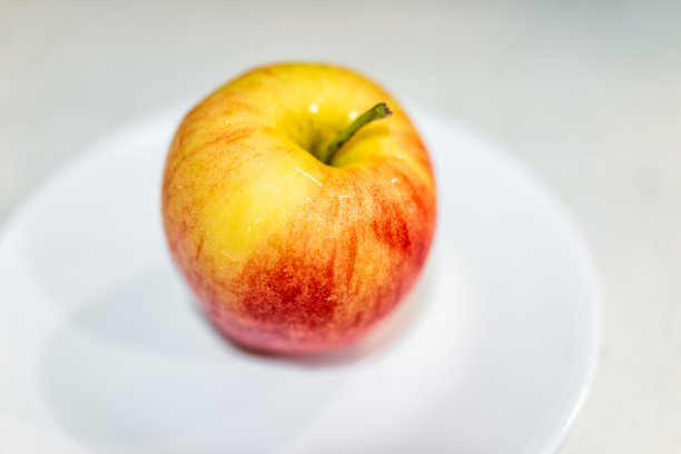 一个洗条纹黄红色gala或富士苹果微距特写纹理在白色盘子工作室拍摄的桌子上与彩色皮肤的变化图片下载