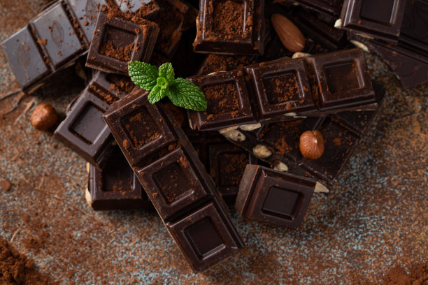 黑牛奶巧克力，黑色背景上撒有可可粉的坚果。图片下载