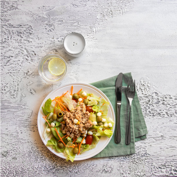 俯视图与经典的金枪鱼沙拉，不同的生菜，一杯水和餐具。健康饮食理念图片下载