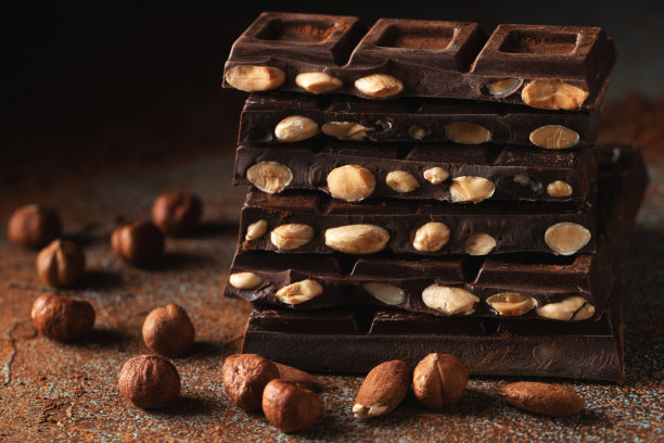 黑牛奶巧克力，黑色背景上撒有可可粉的坚果。图片下载