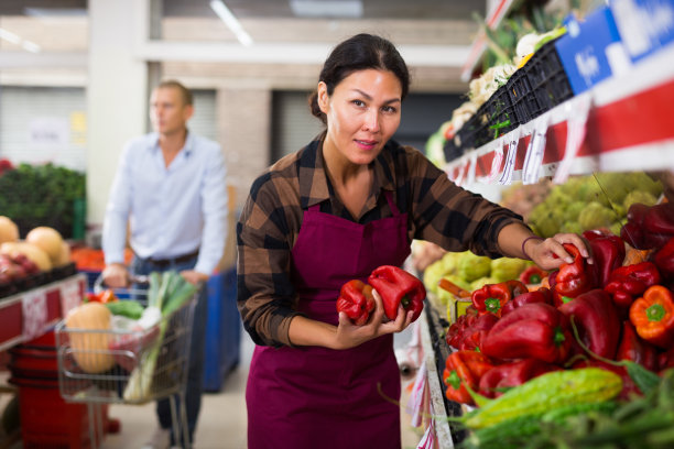 女售货员在市场货架上摆放水果和蔬菜图片下载