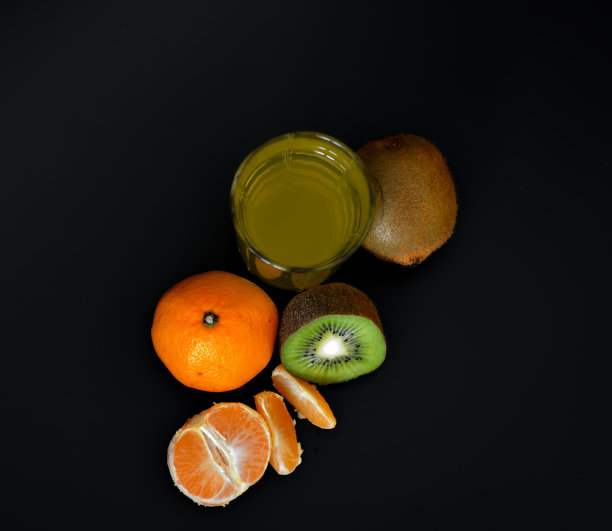 一杯黑色背景的果汁，旁边是几片成熟的橘子和猕猴桃。图片下载