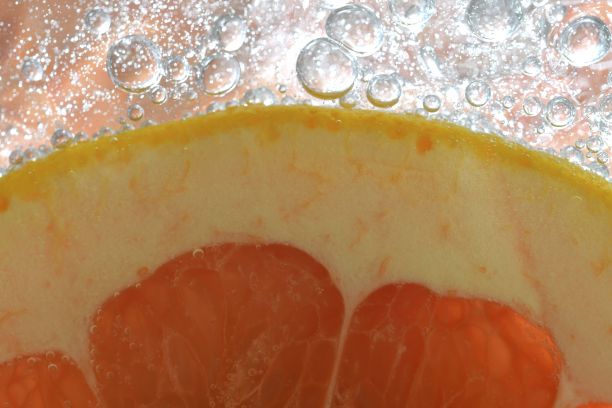 红色葡萄柚切片，白底水。柚子在有气泡的液体中的特写。将红熟葡萄柚切片放入水中。水果在水中的微距图像图片下载