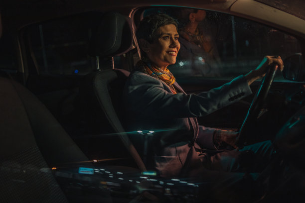 一个成熟的女人在晚上开车，城市的灯光和其他汽车在车窗上刺眼图片下载