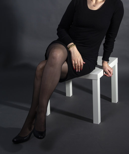 女人在短黑色连衣裙坐在白色小桌子对深灰色背景图片下载