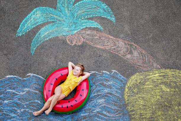 快乐的小学前班女孩在泳装充气环与海，沙子，手掌用彩色粉笔涂在沥青上。可爱的孩子与玩粉笔画的乐趣。夏天，假期，夏天图片下载