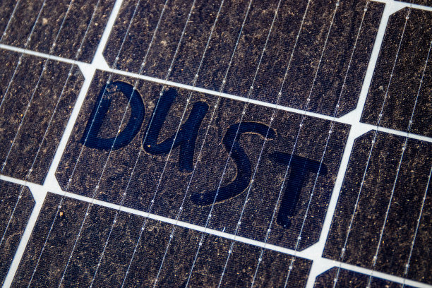 一块用手指写着“灰尘”的脏太阳能电池板。在灰尘条件下太阳能组件效率的概念。图片下载