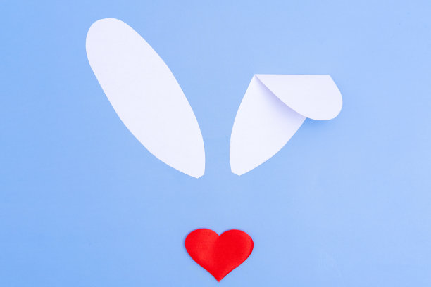 创意贺卡。模仿复活节兔子。红色的心代替鼻子，蓝色背景上的白纸耳朵图片下载