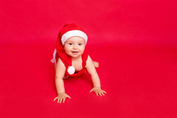 快乐的小婴儿六个月大，戴着圣诞老人的帽子，爬在红色孤立的光电电话上，文字空间，新年和节日的概念图片下载