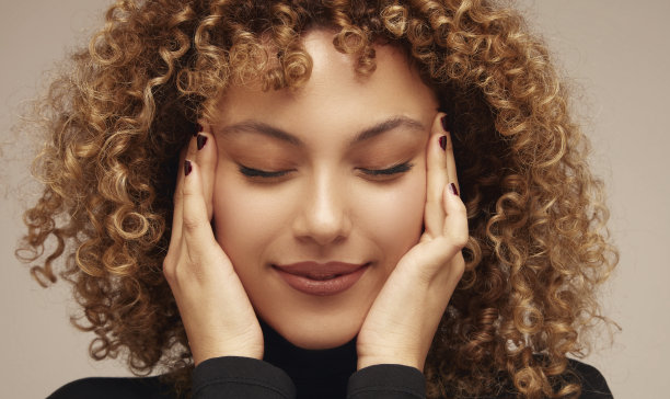 特写，卷发年轻女子微笑，她的手在她的太阳穴。图片下载