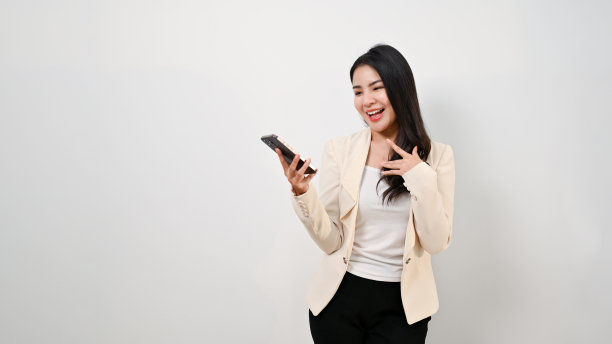 微笑的亚洲女商人站在一个孤立的背景下使用她的智能手机。图片下载