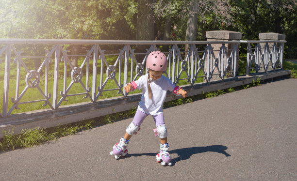 夏天，小女孩带着头盔在公园里滑直排旱冰鞋。儿童锻炼休闲户外体育活动游戏。图片下载