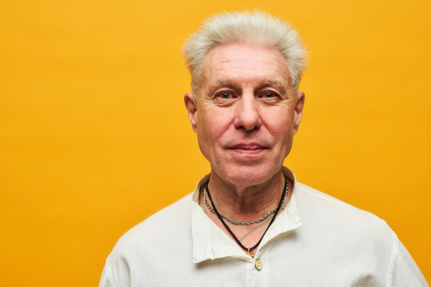 白发老人在黄色背景下看着相机图片下载