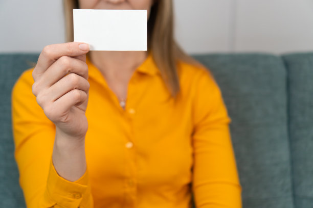 一个戴眼镜、穿橙色衬衫的女人手里拿着一张白色名片的特写。专家提供服务图片下载