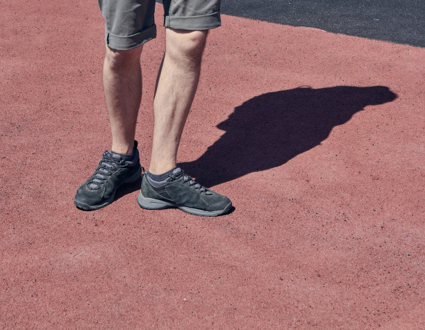 一个穿着超短裤和黑色运动鞋的男人的腿。红色和棕色沥青背景。跑步和步行的概念。穿着黑色运动鞋的年轻人的腿。图片下载