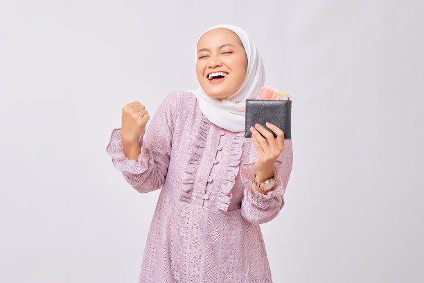 兴奋的年轻美丽的亚洲穆斯林妇女戴头巾和紫色连衣裙持有钱包的全部现金和庆祝成功孤立在白色工作室背景图片下载