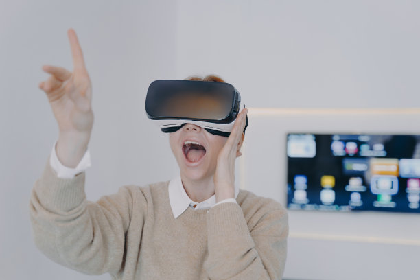 年轻兴奋的女子在VR耳机用手指触摸虚拟按钮指向。图片下载