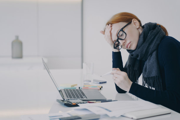 秘书生病了。年轻的白人妇女在办公室拿着体温计，但在做她的工作。图片下载