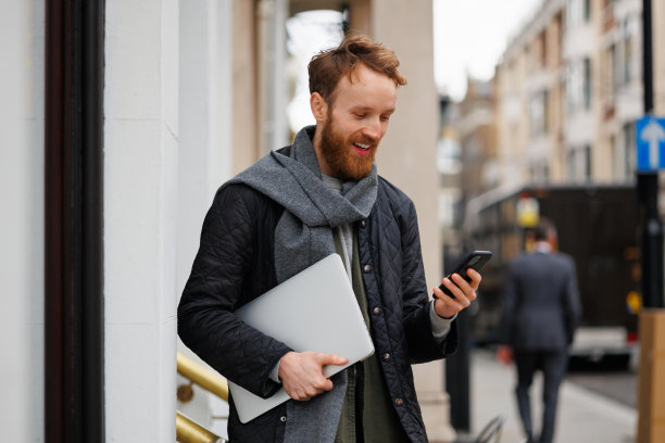 一个快乐的商人，手里拿着笔记本电脑和智能手机站在一个大城市的街道上图片下载